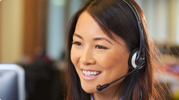 An Asian woman is working as a customer service representative. She is wearing a headset with a desktop computer in front of her.